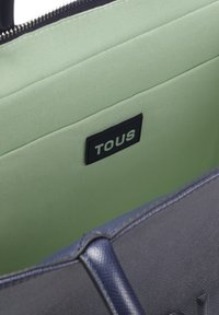 Granatowa torebka z teksturowanym wykończeniem, zielonym wnętrzem i czarną metką z logo "TOUS". Zamek błyskawiczny na górze.