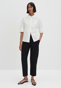 Witte korte mouwen overhemd met kraag van textuurstof en een knoopsluiting aan de voorkant, gecombineerd met zwarte op maat gemaakte broek en zwarte sandalen met bandjes.