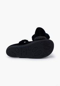 Zapato negro de terciopelo sin cordones con una suela texturizada que presenta patrones de tracción de goma. Notables acentos de correa trenzada en la parte frontal.