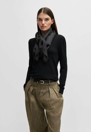 Black knitted sweater, gray scarf with frayed edges, beige pleated trousers, and a black belt with a gold buckle. Neutral background.