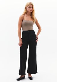 Zwarte wijde broek met hoge taille, voorzien van voorzakken en subtiele stikseldetails, gecombineerd met een aansluitend tanktop.