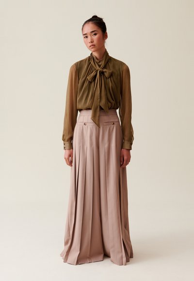 Blusa a cuadros verde oliva con un lazo, combinada con una falda larga plisada beige con bolsillos laterales y detalles en dorado.