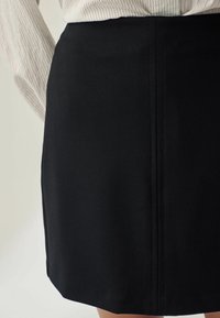 Sort nederdel lavet af glat stof med lige snit, der har subtile syning detaljer og en ren kant. Stylized med en stribet skjorte.
