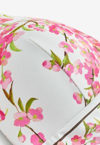 Țesătură albă cu un model floral de flori de cireș roz, brodat într-o formă curbată și căptușită.