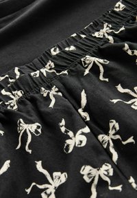 Black fabric with white bow patterns, featuring an elastic waistband and soft texture. Close-up view highlights design details and stitching.