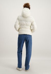 Witte pufferjack met een capuchon, met een gewatteerd ontwerp en geribde manchetten. Gecombineerd met blauwe jeans en witte sneakers.