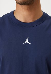Sötétkék pamut póló, amelyen a mellkas közepén egy fehér Air Jordan logó található. Kerek nyakkivágás és rövid ujjú. Sima textúra.