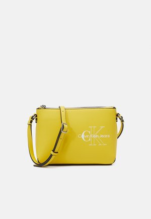 Żółta torba na ramię Calvin Klein Jeans z regulowanym paskiem i srebrnym zamkiem na białym tle.