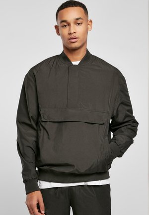 Sort vindjakke med høj krave, frontlomme med flap og elastiske manchetter. Fremstillet af glat, let materiale med et minimalistisk design.
