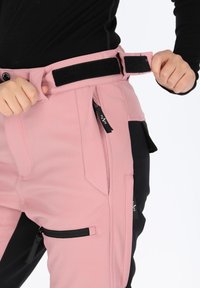 Pants featuring a pink fabric with a smooth texture, black accents, multiple pockets, and a wide adjustable velcro belt.