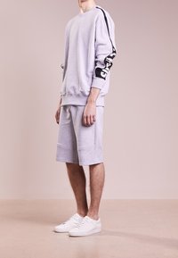 Felpa grigia chiara con striscia laterale nera a motivo, abbinata a pantaloni corti grigi coordinati e sneakers bianche. Look informale e vestibilità rilassata.