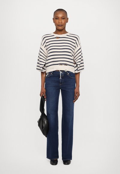 Maglione a righe in crema e blu navy, con orlo cropped e maniche oversize, abbinato a jeans svasati blu scuro e con una borsa nera.