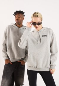 Grey hoodies with front pockets, featuring the text "Groove Bloom" in black. One model wears black sunglasses; both wear casual denim.