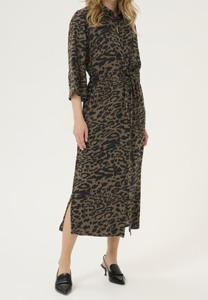 Frau trägt ein braun-schwarzes Midikleid mit Leopardenmuster, dreiviertellangen Ärmeln, Taillengürtel, Schlitz vorne und schwarzen spitzen Slingback-Schuhen.