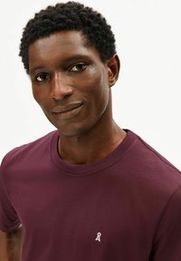 Bordeauxrode katoenen T-shirt met een ronde hals en een klein wit logo op de linkerborst. Zachte textuur, casual pasvorm.