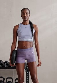 Nike Pro urheiluliivi vaalealaventelissa, yhteensopivat shortsit ja painolaatta. Sileä kangas, kapea muotoilu, hienovaraisia logokoristuksia.