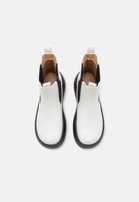 Botas Chelsea blancas con paneles laterales elásticos negros, textura suave, punta redondeada, lengüetas de tirón y un forro interior acolchado.
