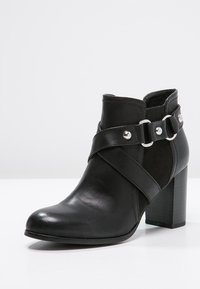 Czarne botki za kostkę o gładkiej skórzanej powierzchni, z ozdobnym paskiem z metalowymi akcentami i grubym, wysokim obcasem.