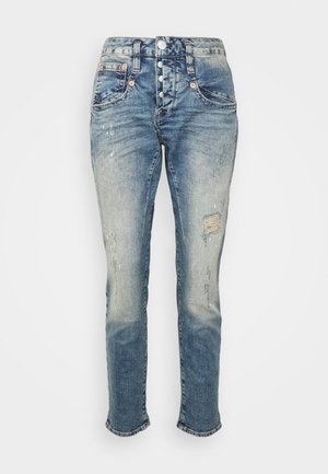 Vaaleansiniset farkut, joissa on korkea vyötärö, viisi nappia kiinnityksessä, kulutetut yksityiskohdat ja hieman kapeneva lahje. Revähtänyt helma nilkoissa.