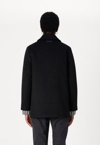 Zwarte jas met een kraag, achteraanzicht toont lange mouwen en een gestreepte stofdetail bij de manchetten. De stof lijkt glad en gestructureerd.