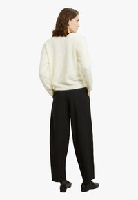 Maglione bianco e peloso con maniche lunghe abbinato a pantaloni neri larghi e scarpe nere. Il completo presenta una vestibilità comoda e una texture morbida.