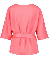 Korallblus med vida ärmar och draperad rygg, med ett fast orange bälte i midjan för extra form och detalj. Slät textur.