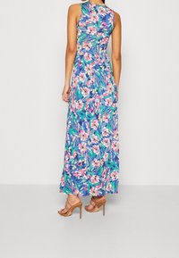 Maximehdress, joka sisältää värikkään kukkakuosin sinisellä taustalla, olkaimeton malli ja liikkuva siluetti, yhdistettynä nude korkokenkiin.