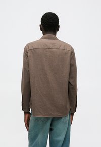 Καφέ, υφασμάτινο πουκάμισο με γιακά, μακριά μανίκια και κανονική γραμμή, ορατό από πίσω. Μαλακό ύφασμα με διακριτές λεπτομέρειες σχεδίου.