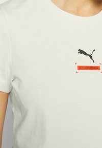 Bílý bavlněný tričko s černým skákajícím logem pumy a červeným nápisem "BETTER SPORTSWEAR". Krátké rukávy a kulatý výstřih.