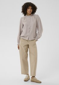 Lys grå skjorte med puffede ærmer, tekstureret stof og en flæsenedrinning, parret med beige brede bukser og brune sneakers.