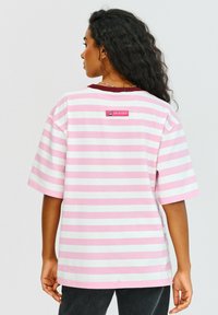 Pruhované tričko s růžovými a bílými barvami, krátkými rukávy, kulatým výstřihem a malou nášivkou s logem "FRIENDS" na zadní straně.