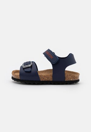 Børns mørkeblå sandal med korkindlæg, justerbar rem foran med spænde og velcrolukning ved anklen mærket Geox, på sort tekstureret sål.