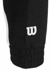 Pantalón atlético negro con franjas laterales blancas, puños elásticos y un logo blanco. La tela parece suave y resistente con un diseño ceñido.