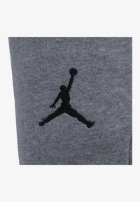 Tejido gris con una textura suave que presenta una silueta del logo Jumpman en negro, representando a un jugador de baloncesto en el aire, situado en el lateral.