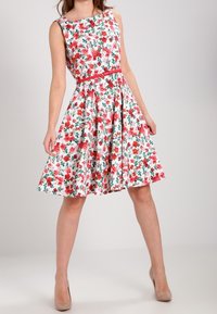 Blumenprint-Kleid mit tailliertem Oberteil, ausgestelltem Rock und rotem Gürtel. Der Stoff hat einen weißen Hintergrund mit roten und grünen Mustern.
