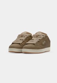 Brown suede sneakers with a rounded toe, beige laces, and a white rubber midsole. Embossed logo on the side and tongue.