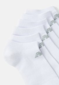 Calcetines blancos hasta el tobillo con parte superior acanalada, que presentan un diseño sutil de logo verde en el lado exterior. Seis pares apilados de manera ordenada.