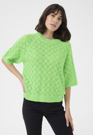 Gebreide trui in scherp groen met een diamanten kantpatroon, korte mouwen en een ribbelachtige ronde halslijn. Draag het met zwarte, strakke broeken.
