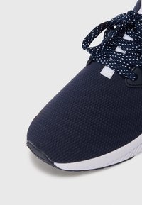 Navy athletic shoe with textured mesh upper, white midsole, and navy polka dot laces. Features a padded collar and rounded toe design.