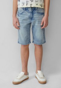 Jasnoniebieskie szorty dżinsowe z postrzępionym dołem, dwoma przednimi kieszeniami i luźnym krojem, zestawione z białymi sneakersami z brązowymi podeszwami.