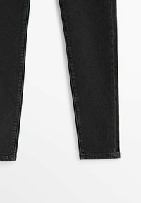 Jean en denim noir skinny montrés de la cuisse à la cheville sur un fond blanc.