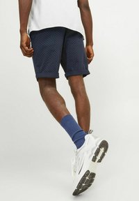 Pantalones cortos navy con lunares blancos, con cinturilla enrollada, combinados con calcetines azules y zapatillas blancas con suelas negras.