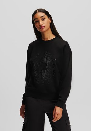 Black sweatshirt featuring a textured design with a sparkling graphic at the center. Long sleeves and ribbed cuffs enhance the fit.