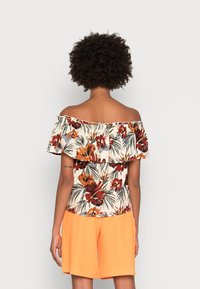 Top épaules dénudées à imprimé floral avec manches volantées, présentant des fleurs rouges et orange sur un fond crème, associé à un short orange.