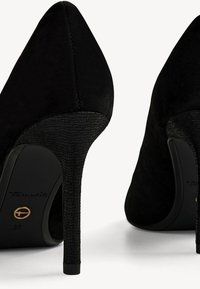 Zapatos de tacón alto negros con punta afilada, hechos de ante con un tacón texturizado. Detalle del logo visible en la suela. Talla 37.