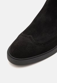 Pantofii din piele de nubuck neagră au o finisare netedă, vârful rotunjit și detalii discrete de cusătură. Beneficiază de o talpă din cauciuc pentru aderență și tracțiune.