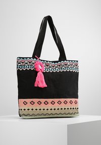 Bolso tote negro con bordado decorativo que presenta patrones en rosa, azul y verde. Incluye un borlas rosa y asas negras resistentes.