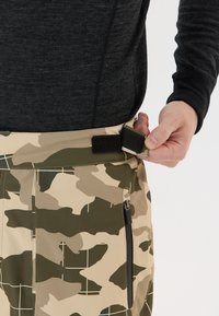 Camouflaged broeken in beige en groen, met een klittenbandsluiting op de taille en een ritszak aan de zijkant. Glad, lichtgewicht materiaal.