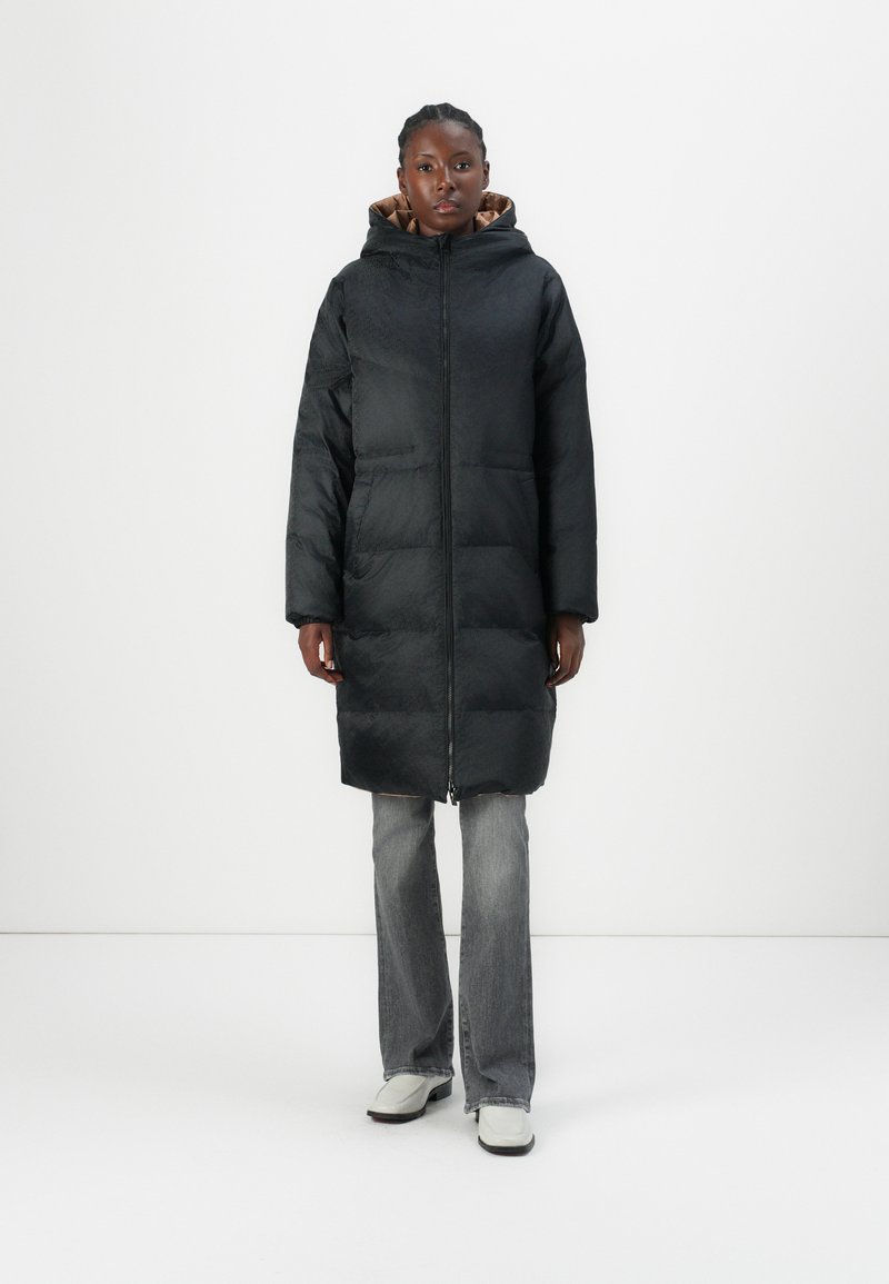 Black long puffer coat with a zip closure and a hood, featuring a smooth texture and two front pockets. Paired with light gray flared jeans and shoes.