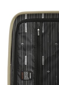 Interior de maleta negra con bolsillo de malla con cremallera, con un patrón de líneas blancas y motivos de aviones, y una etiqueta con instrucciones de cuidado.